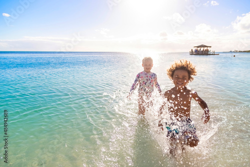 A Cute diverse boy and little girl running and splashing together in the Caribbean ocean in the late afternoon while on a family vacation