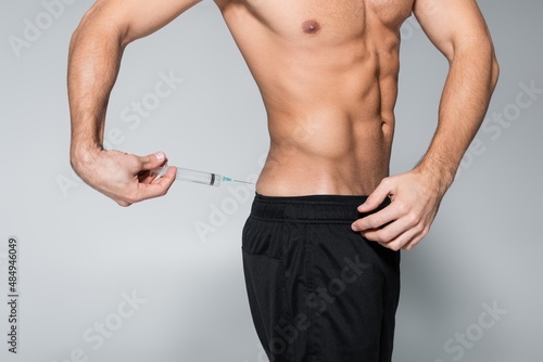 cropped view of shirtless and muscular sportsman injecting himself with steroids on grey.
