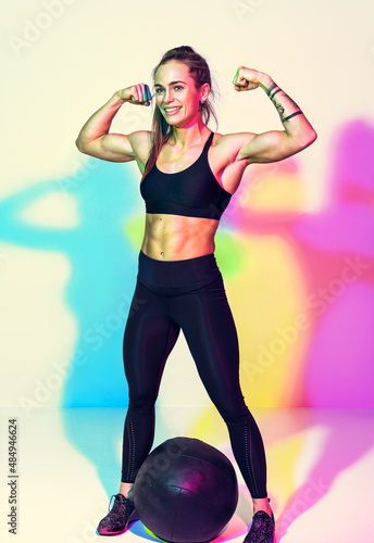 Strong woman after workout with med ball. Photo of woman with perfect physique on white background with effect of rgb colors shadows. Strength and motivation.