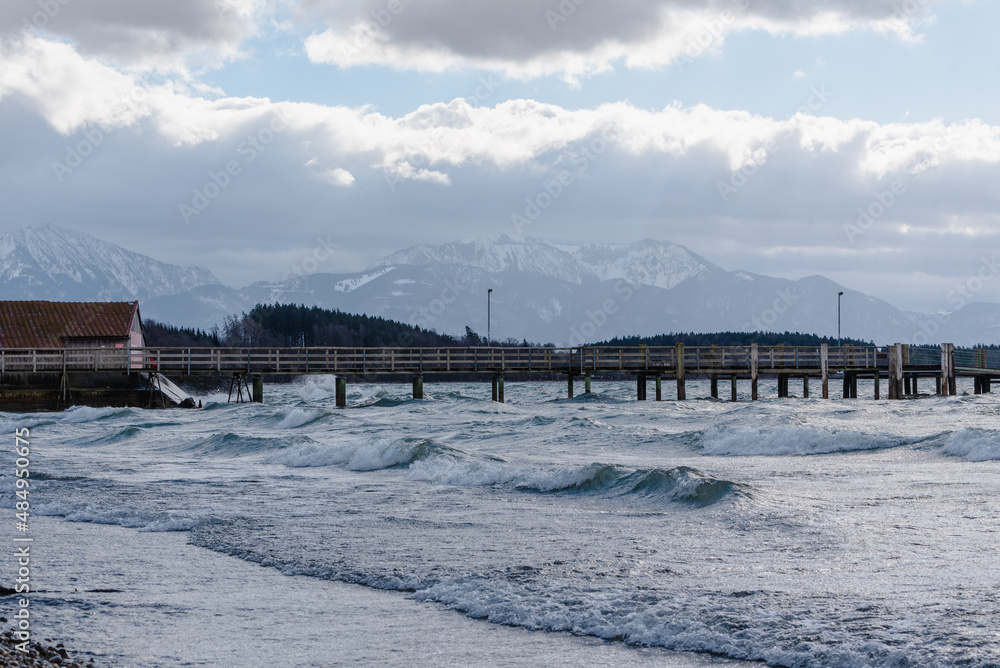 Dampfersteg aus Holz im Chiemsee bei Sonnenschein und Sturm mit brechenden wellen , mit Alpen im Hintergrund , Wolken udn blauem Himmel Dampfersteg aus Holz im Chiemsee bei Sonnenschein und Sturm mit brechenden wellen , mit Alpen im Hintergrund , Wolken udn blauem Himmel