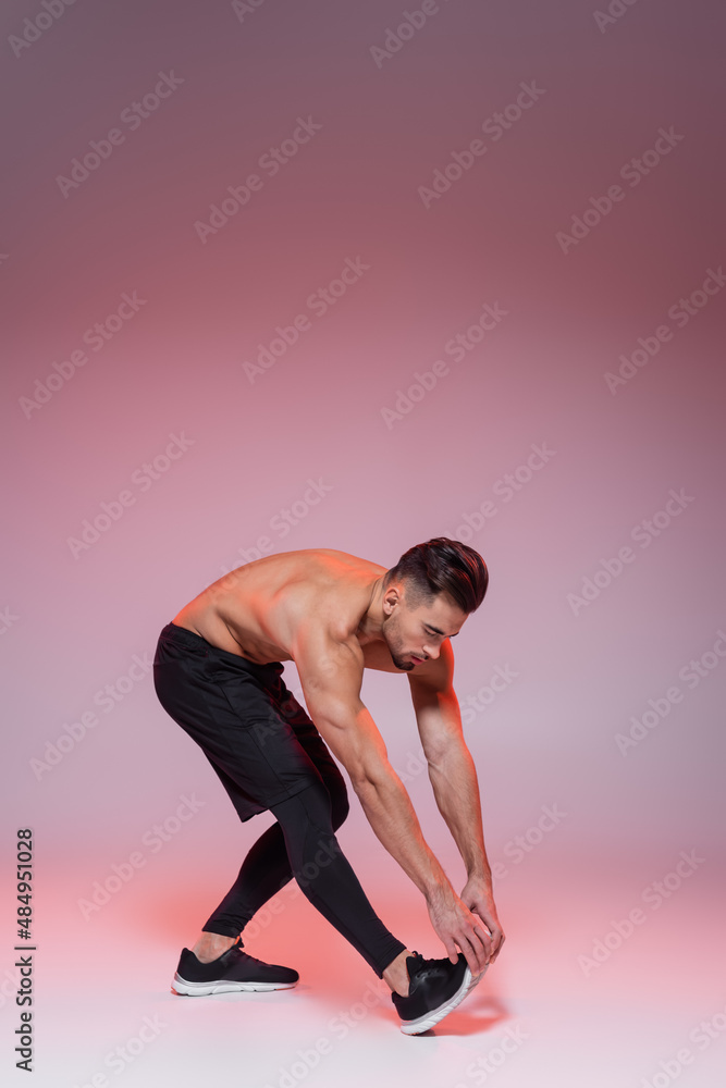 shirtless sportsman leaning while stretching on grey and pink. shirtless sportsman leaning while stretching on grey and pink.