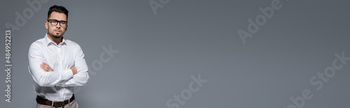 bearded businessman in white shirt and glasses standing with crossed arms isolated on grey, banner. © LIGHTFIELD STUDIOS