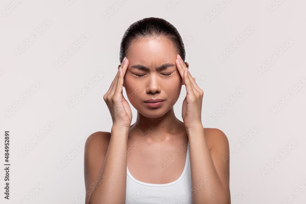 Unhappy millennial chinese lady massaging her temples Unhappy millennial chinese lady massaging her temples