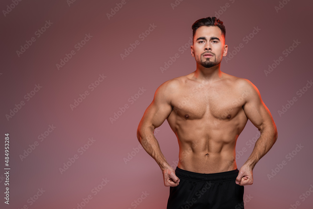 red lighting on strong man with muscles posing on pink and grey.