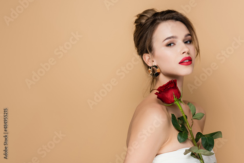 Fényképezés pretty young woman in strapless top holding red rose and looking at camera isolated on beige