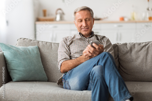 Senior Male Using Smartphone Texting Sitting On Sofa At Home © Prostock-studio