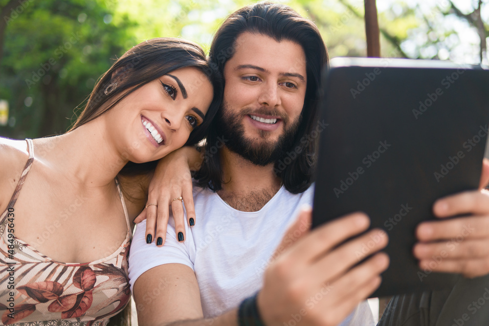 pretty couple using tablet for entertainment in the park pretty couple using tablet for entertainment in the park