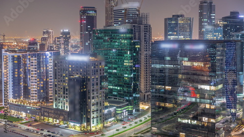 Business Bay Dubai skyscrapers with city lights reflected on glass aerial night timelapse.