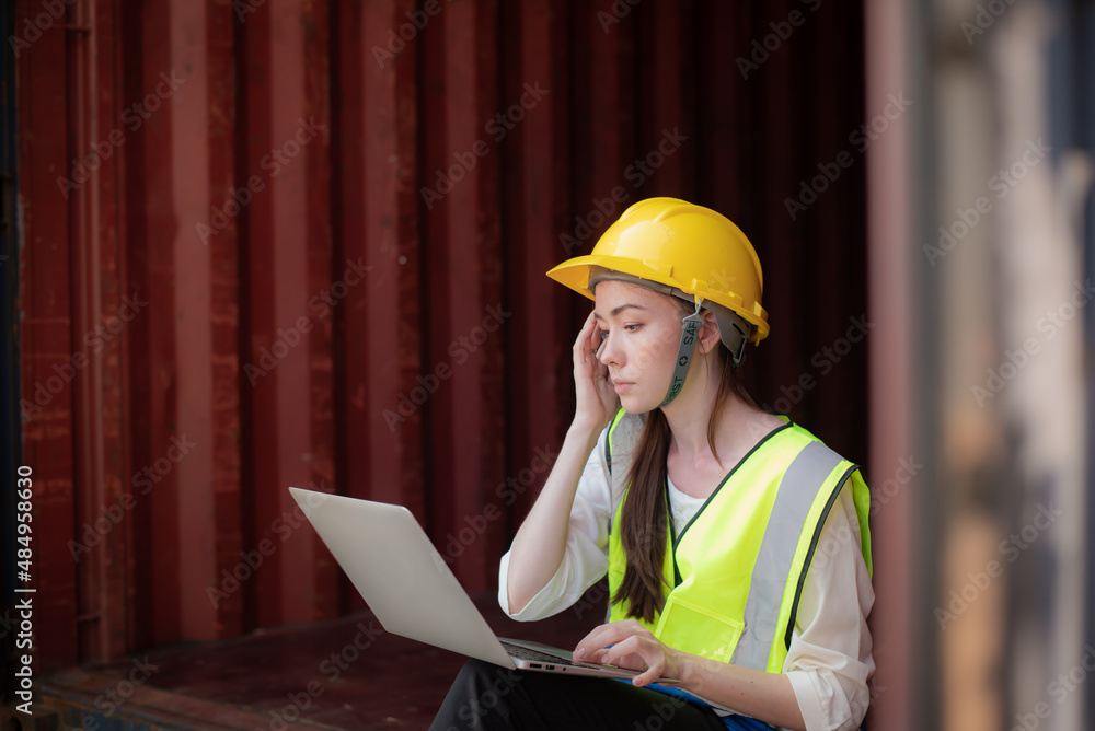 Fototapeta premium Young Caucasian women worker sitting at work with a laptop with a serious expression on her face. to inspect the stock of goods at the containers before delivering them to overseas customers