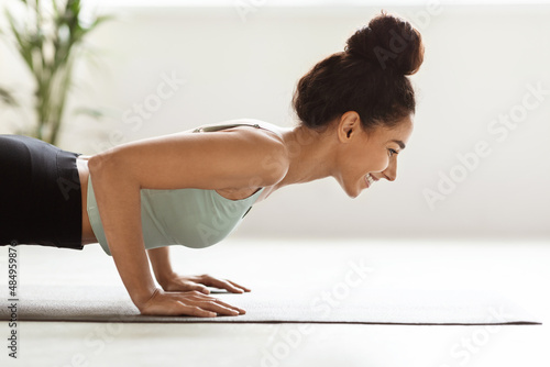 Side View Of Young Woman Doing Plank Exercise And Push Ups Indoors photo