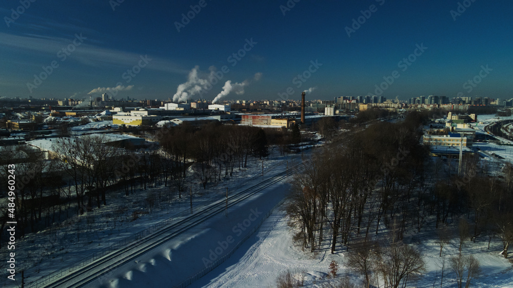 Industrial area on the outskirts of the city. Factory buildings are covered with snow. Factory pipes are visible. Winter industrial landscape. Aerial photography.