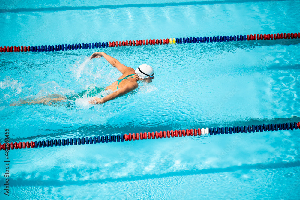 Wide shot of a Caucasian female athlete doing the butterfly stroke to swim the pool.