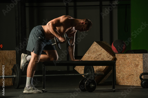Athletic caucasian man doing a dumbbell triceps kickback with his right arm on a horizontal bench.