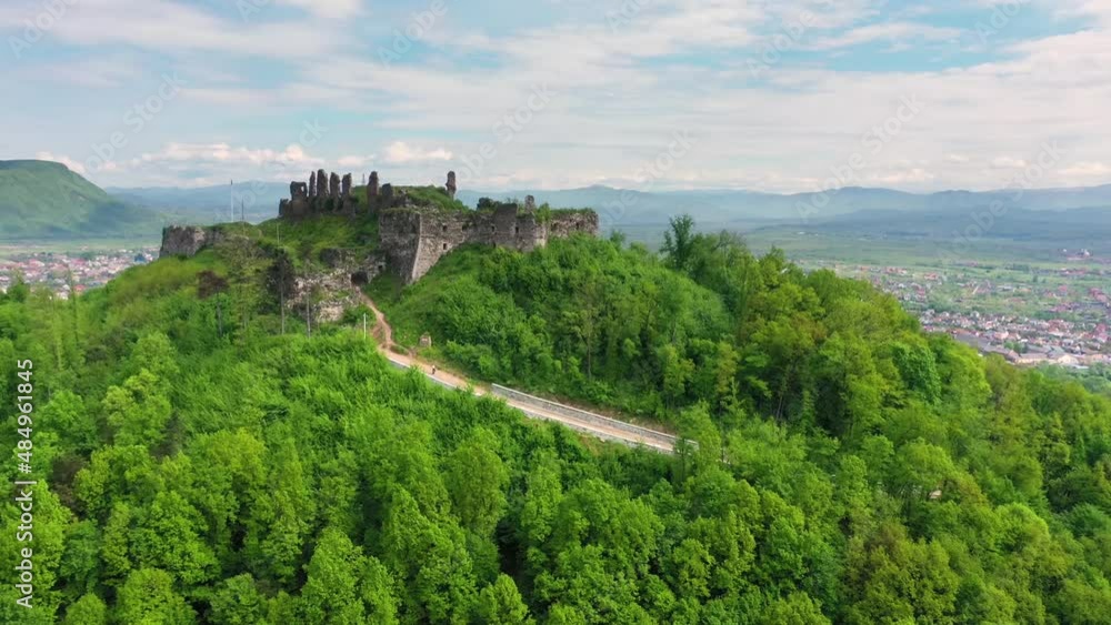 Flight of a quadrocopter over the ancient castle of Ukraine in Transcarpathia, surrounded by the city of Khust. Ancient remains of a wall and a tower on a high mountain overgrown with forest Flight of a quadrocopter over the ancient castle of Ukraine in Transcarpathia, surrounded by the city of Khust. Ancient remains of a wall and a tower on a high mountain overgrown with forest