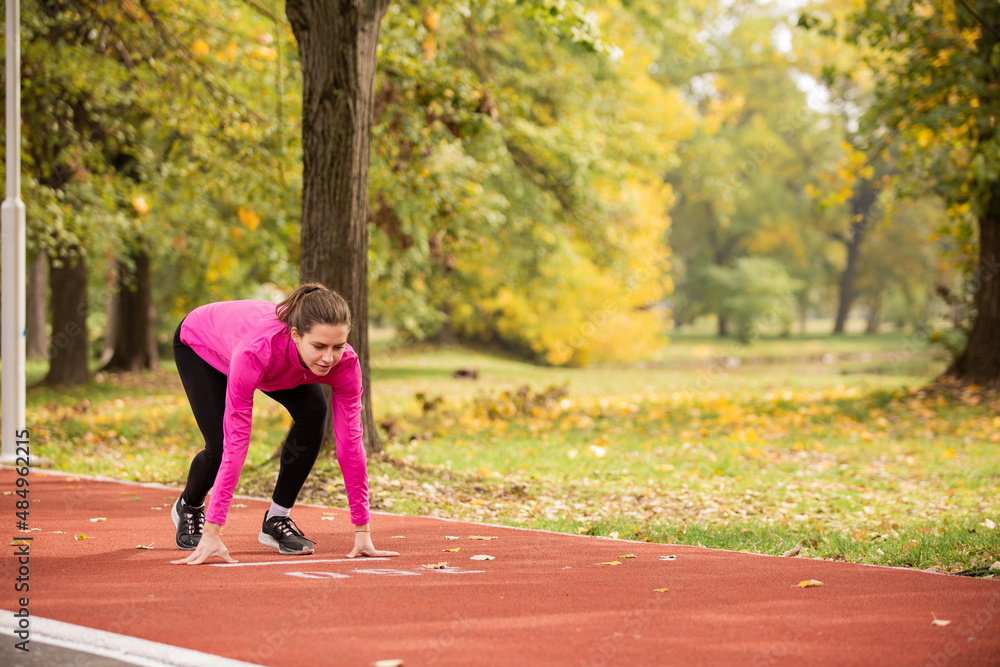 Preparing for her run training alone on the red track while focusing, in the park Preparing for her run training alone on the red track while focusing, in the park