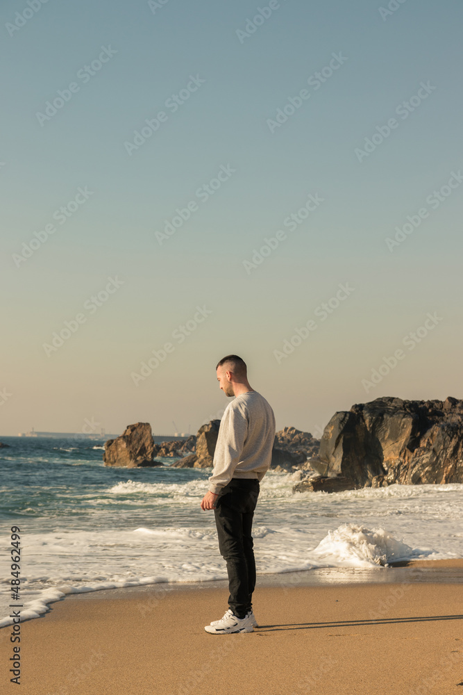Full-length man thinking on the shore of the beach with rocks in the background, picture taken in Porto, Portugal