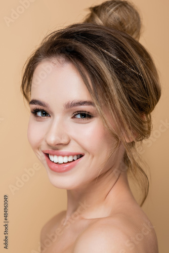 close up view of charming woman with natural makeup smiling at camera isolated on beige.