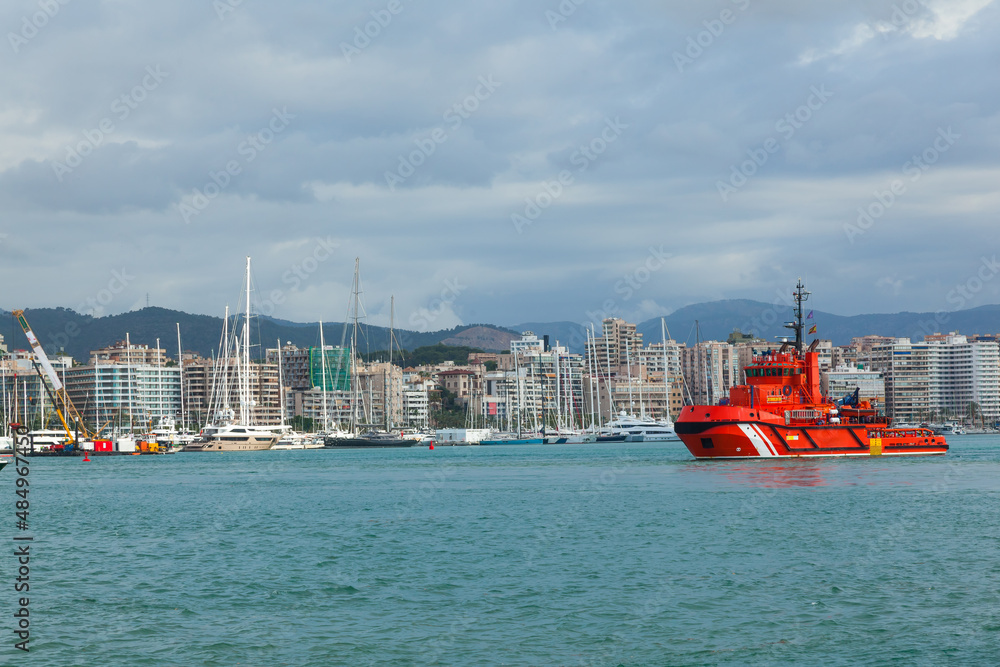 Red tug in the bay of Palma de Mallorca. On the coast of the house, at the pier moored yachts.