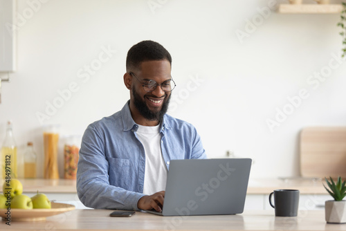 Satisfied young african american bearded man with glasses working on laptop