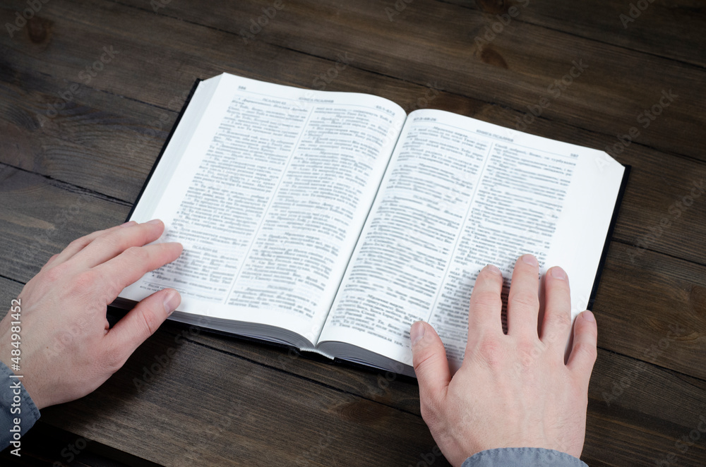 Naklejka premium Prayer. Open Bible. Hands folded in prayer. The man is praying. Hands on the table. 