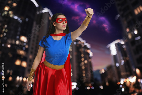 Confident young woman wearing superhero costume and beautiful cityscape in night on background