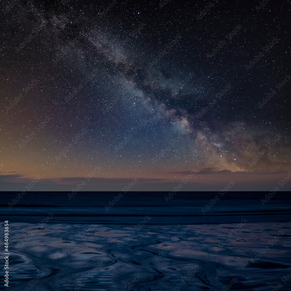 Digital composite image of Milky Way over Absolutely beautiful landscape images of Holywell Bay beach in Cornwall UK during golden hojur sunset in Spring