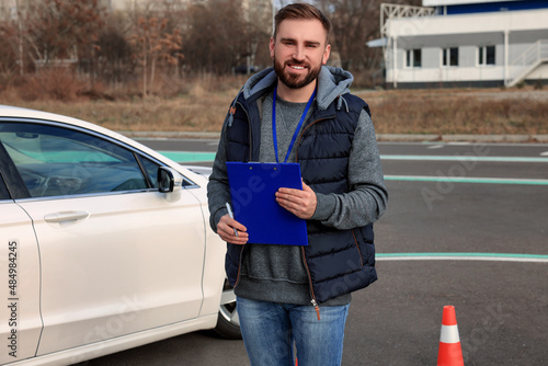 Instructor with clipboard near car outdoors. Driving school exam