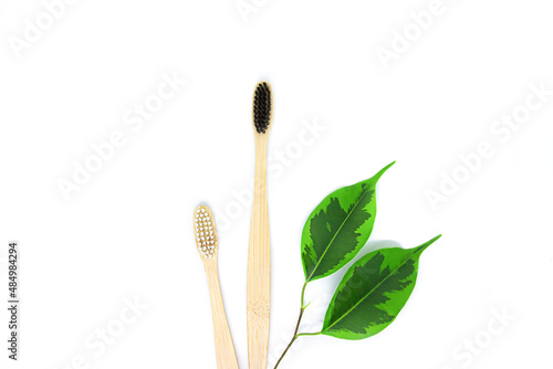 eco-friendly bamboo toothbrushes in black and white and a twig with green leaves lie on a white background. Flat lay, top view. Copy space. Zero waste personal care product, dental care