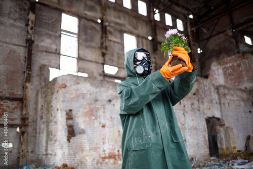 A dosimetrist scientist radiation inspector in protective clothing and a gas mask examines the danger zone. Close-up. Flower. Ecological catastrophy photo