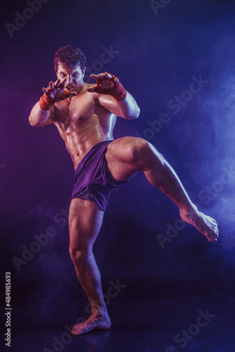 Full size of kickboxer fighter who delivering knee hit isolated on smoke background. mixed media 