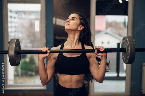 Attractive young woman training in the gym and using barbell