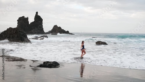 Beautiful woman in swimming suit walking on a black sandy beach in the Canary Islands, Tenerife photo