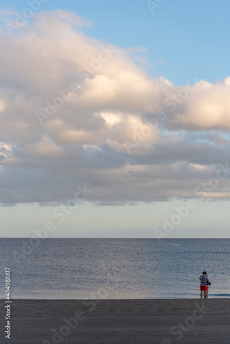 Mujer joven de espaldas en la playa durante un atardecer de verano con el mar en calma en Lanzarote Islas Canarias
