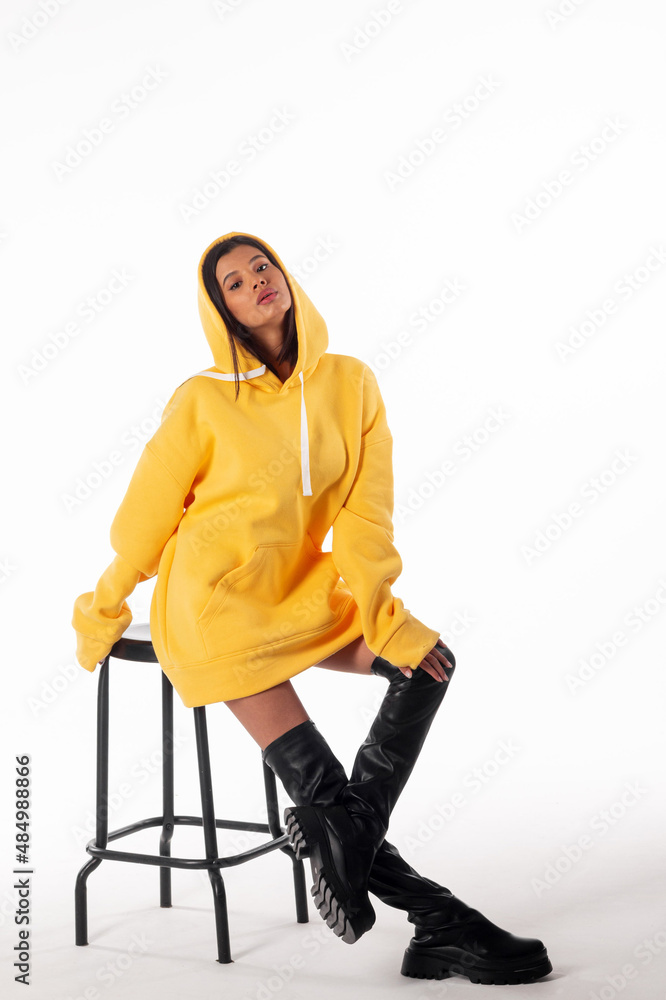 Attractive woman of Latin appearance wears a yellow hoodie on a white background. The girl looks sexy and happy. The elegant brunette is wearing a bright sweatshirt. All-season clothing Attractive woman of Latin appearance wears a yellow hoodie on a white background. The girl looks sexy and happy. The elegant brunette is wearing a bright sweatshirt. All-season clothing