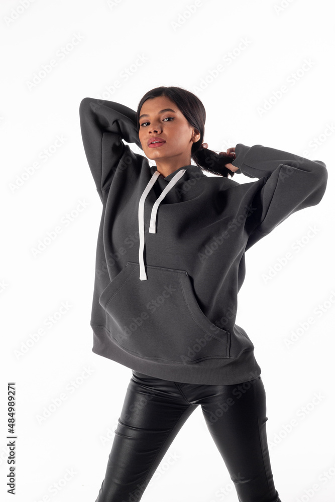An attractive woman of Latin appearance wears a gray hooded hoodie on a white background. The girl looks sexy and happy. The elegant brunette is wearing a dark sweatshirt. All-season clothing An attractive woman of Latin appearance wears a gray hooded hoodie on a white background. The girl looks sexy and happy. The elegant brunette is wearing a dark sweatshirt. All-season clothing
