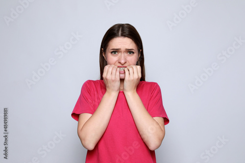 Young woman biting her nails on light grey background