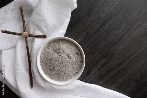 White bowl of ashes with white linen and small christian cross on a dark wood background with copy space photo