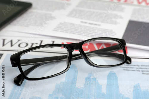 Stylish glasses on newspaper pages, closeup view