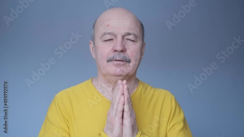 Senior man over isolated blue background keeps palm together.