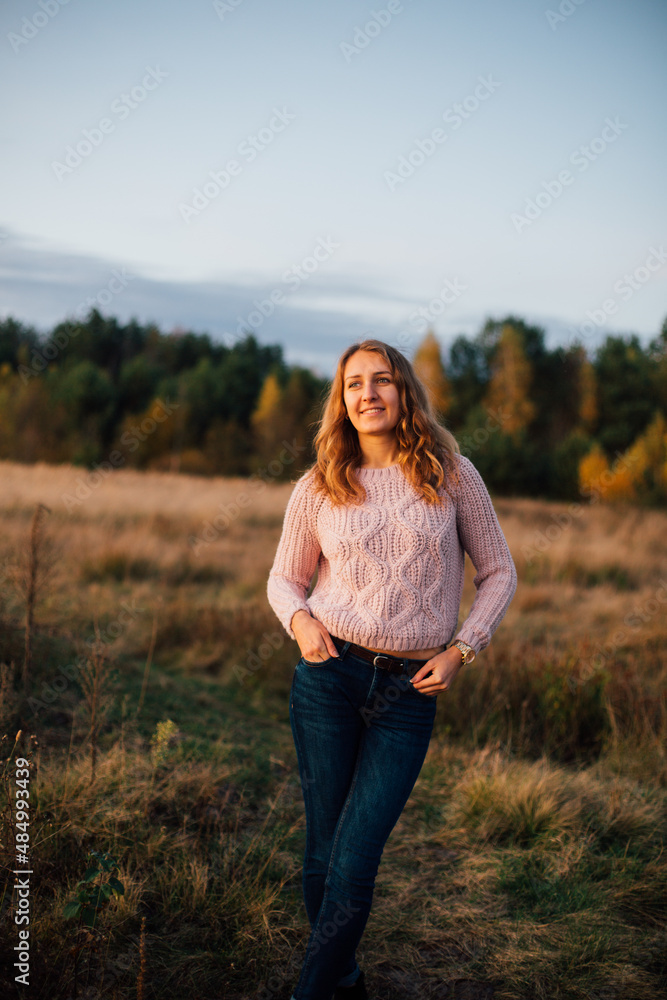 Beautiful girl in a pink sweater on a background of autumn forest. Warm autumn evening