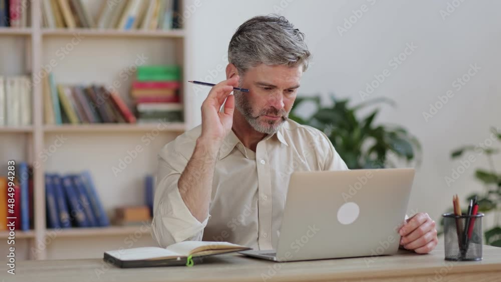 A serious man sits at home with a laptop, makes notes in a notebook. A serious man sits at home with a laptop, makes notes in a notebook.