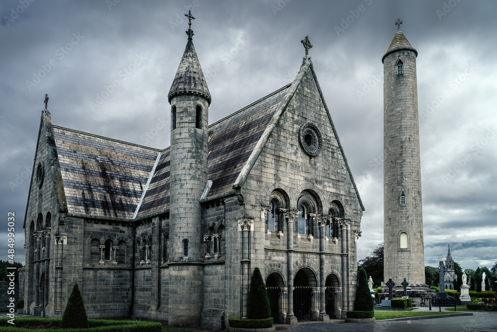 Fototapeta premium Beautiful, ancient mausoleum with Celtic cross and Round Tower in Glasnevin Cemetery, dramatic storm sky in background, Dublin, Ireland