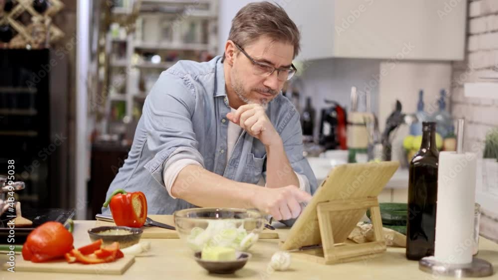 Man cooking in kitchen at home reading recipe on tablet. Healthy eating, diet, cooking application. Man cooking in kitchen at home reading recipe on tablet. Healthy eating, diet, cooking application.