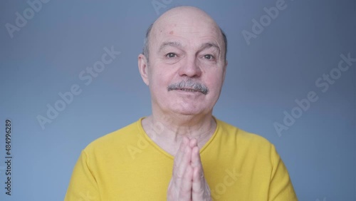 Senior man over isolated blue background keeps palm together.