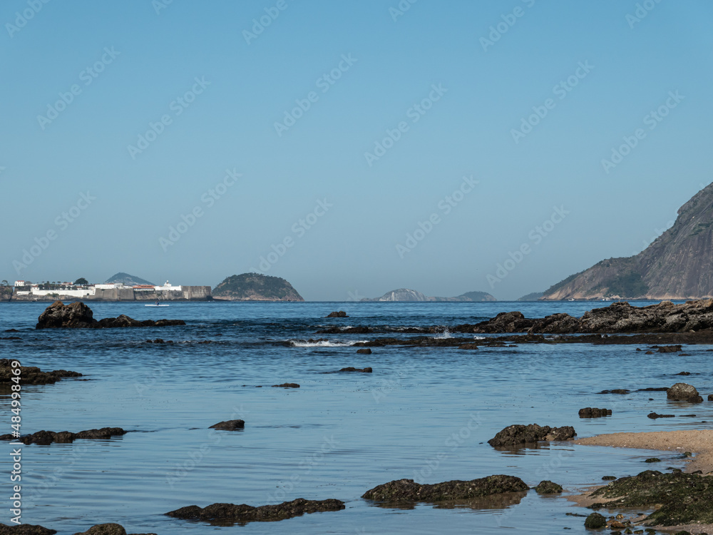 Icaraí Beach in Niteroi city, Rio de Janeiro state, Brazil, with Santa Cruz Fortress on the horizon in a sunny day and blue sky.