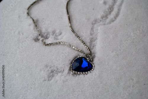 Close-up of the Heart of The Ocean necklace on snow. Titanic necklace. Blue diamond in a heart shape. Diamond necklace.