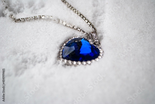Close-up of the Heart of The Ocean necklace on snow. Titanic necklace. Blue diamond in a heart shape. Diamond necklace.
