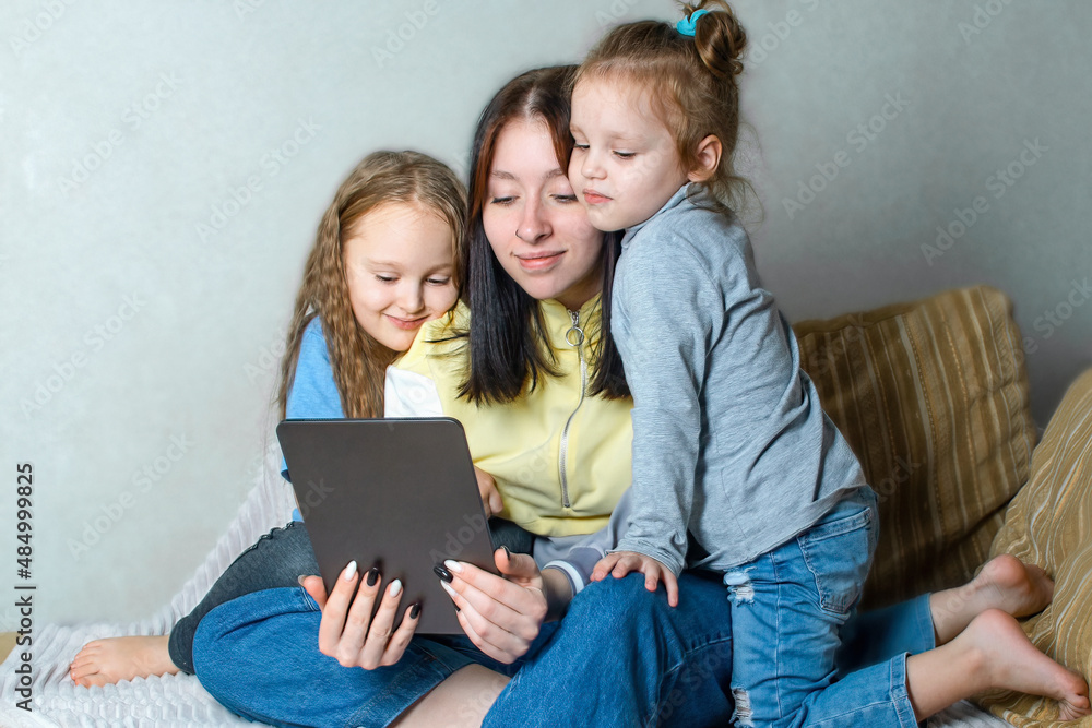 Three sisters have fun together at home on the couch, chatting and watching something online on the tablet, mutual understanding and friendship between relatives in the family. Three sisters have fun together at home on the couch, chatting and watching something online on the tablet, mutual understanding and friendship between relatives in the family.