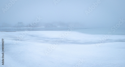 Minimalist winter seascape of the frozen snow-covered coastal beach on Cape Cod. Calm zen-like Asian painting style soft image with space for texts and design.