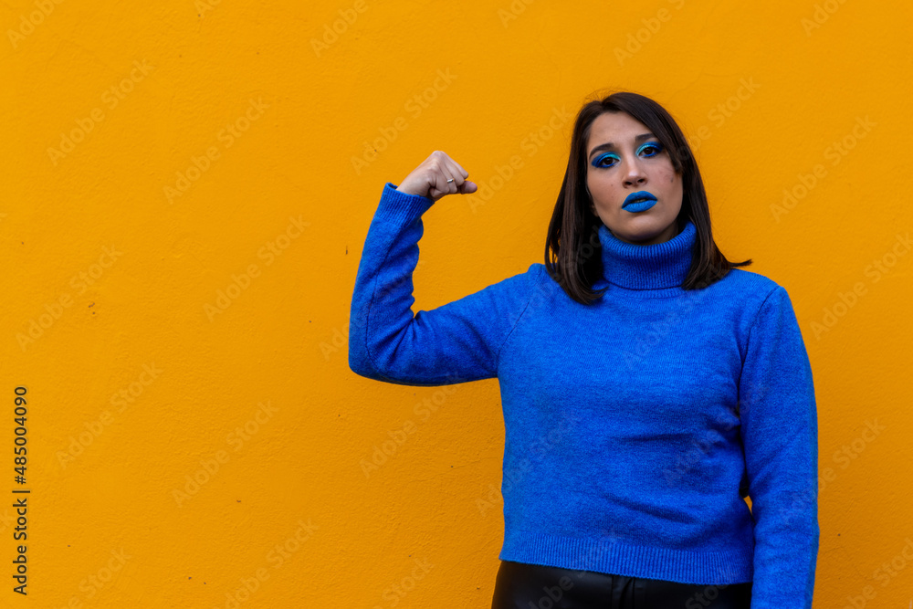 portrait of a serious young woman with the girl power symbol on a yellow background.feminist, march 8,women's day concept portrait of a serious young woman with the girl power symbol on a yellow background.feminist, march 8,women's day concept